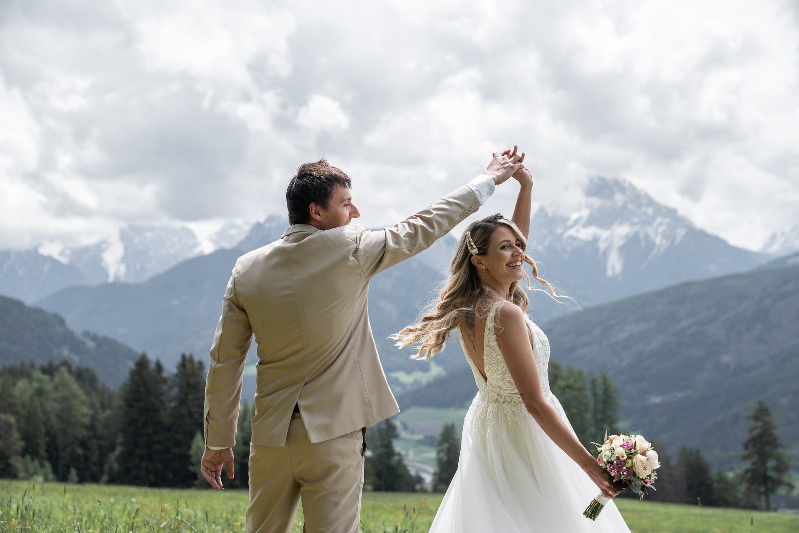 Groom twirling bride in a wildflower meadow, Dolomites behind